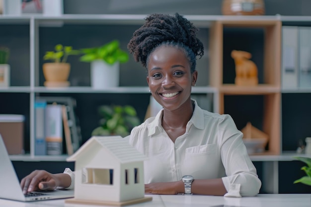 Afrikanische Geschäftsfrau präsentiert ein Hausmodell am Büro-Schreibtisch