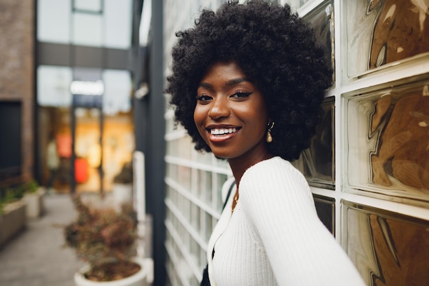 Afrikanische junge Frau, die glücklich aussieht, während sie gegen die Glaswand posiert