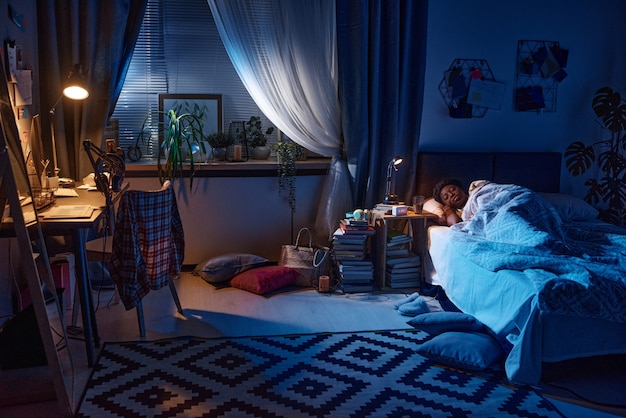 Afrikanische junge Frau, die nachts im Bett in ihrem Schlafzimmer mit Lampe auf dem Tisch schläft