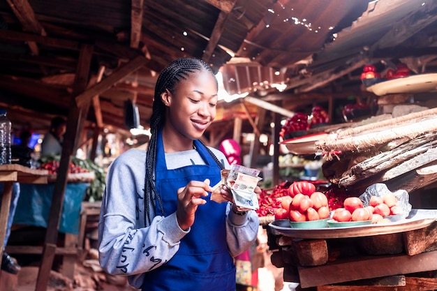 Afrikanische Marktfrau lächelt, während sie Geld zählt, das sie von der Kreditbank erhält