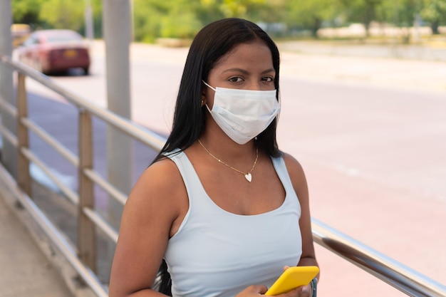 Afrikanische Reisende mit Schutzmaske mit Handy beim Stehen am Busbahnhof