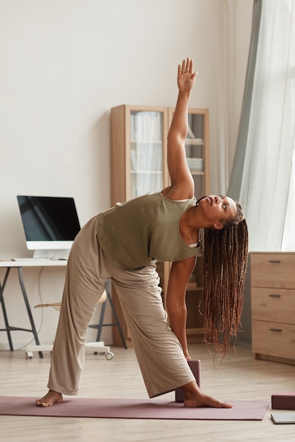 Afrikanische schöne Frau, die auf Übungsmatte steht und Dehnungsübungen im Wohnzimmer zu Hause macht