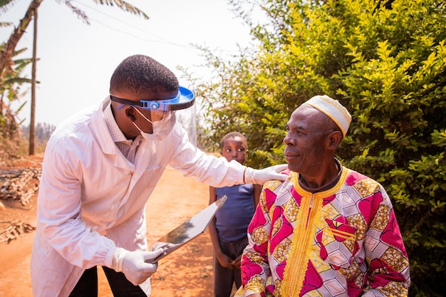 Afrikanischer Arzt besucht einen älteren Patienten und sie unterhalten sich während der ärztlichen Untersuchung Gesundheitsversorgung in Afrika Konzept