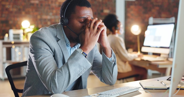 Afrikanischer Callcenter-Mann und Stress durch Computermüde oder Verwechselung mit Panne oder Fehler beim technischen Support. CRM-Berater oder Agent im nächtlichen Telemarketing oder Kundenservice mit Müdigkeit, Burnout oder Ausfall