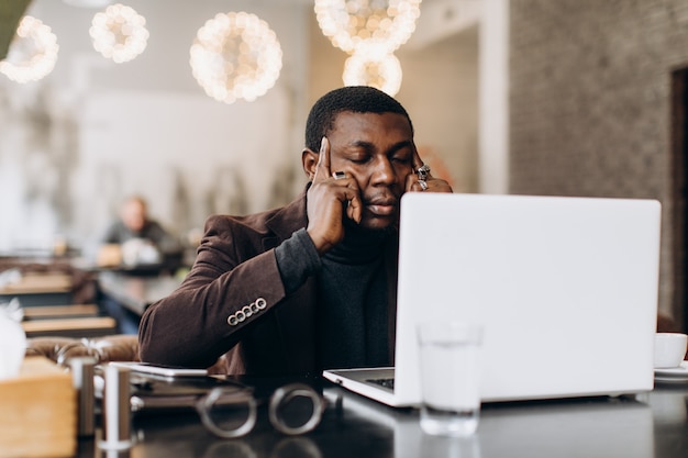 Afrikanischer denkender Geschäftsmann und beim Arbeiten an Laptop in einem Restaurant müde.