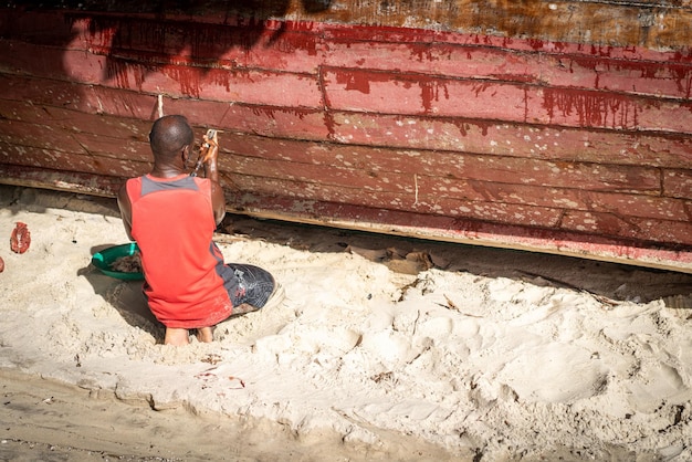 Afrikanischer Fischer am Strand, der sein Boot repariert