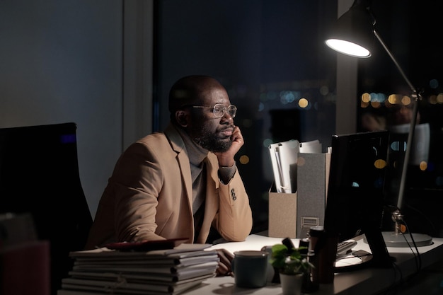 Afrikanischer Geschäftsmann, der am Schreibtisch vor dem Computermonitor sirrt