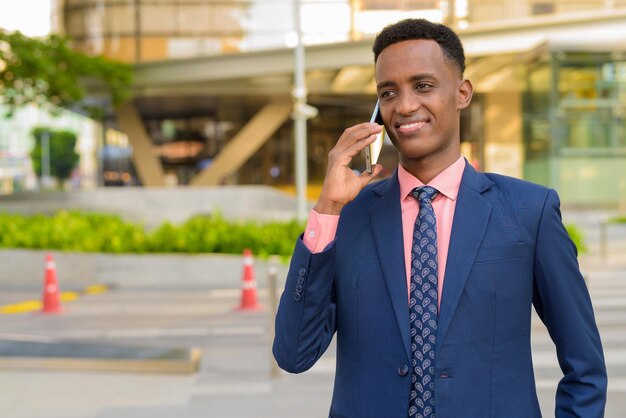 Afrikanischer Geschäftsmann, der Anzug und Krawatte trägt, während er Handy benutzt