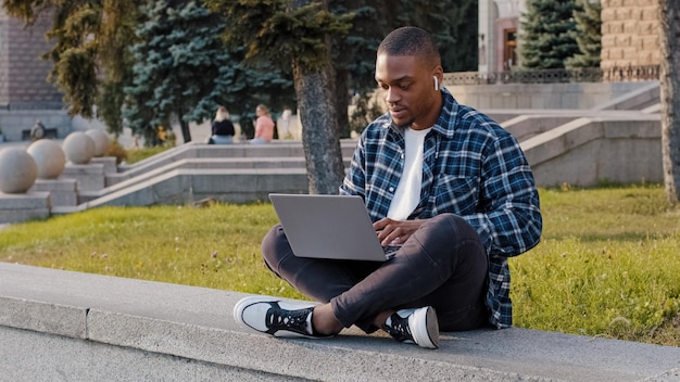 Afrikanischer Geschäftsmann des amerikanischen Studenten, der draußen in der Stadtstraße sitzt und auf dem Laptop arbeitet