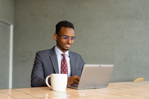 Afrikanischer Geschäftsmann mit Anzug und Krawatte im Café, während er einen Laptop benutzt