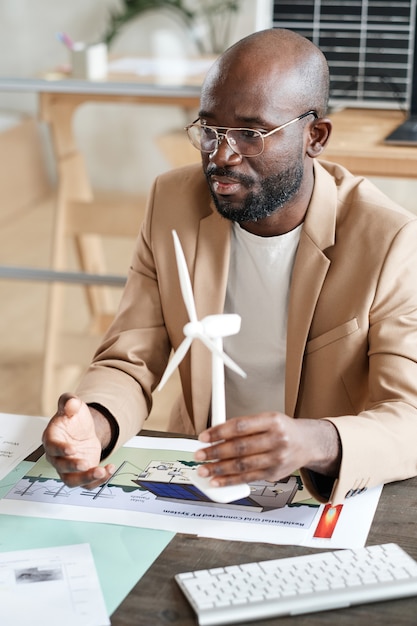 Afrikanischer Ingenieur, der mit Blaupause am Tisch sitzt und ein neues Projekt beim Geschäftstreffen vorstellt