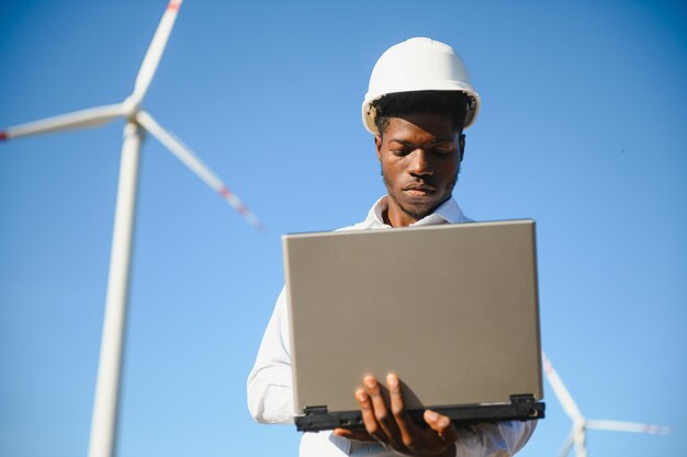 Afrikanischer Ingenieur steht und hält Laptop mit Windkraftanlage