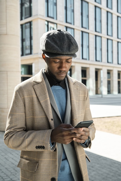 Afrikanischer junger Mann, der eine Nachricht auf seinem Handy eingibt, während er im Freien steht