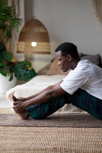 Afrikanischer junger Mann, der in Paschimottanasana oder intensiver Rückendehnungshaltung sitzt, sitzende Vorwärtsbeugehaltung, Übung für Hüften und Wirbelsäule zu Hause. Vertikale Ausrichtung