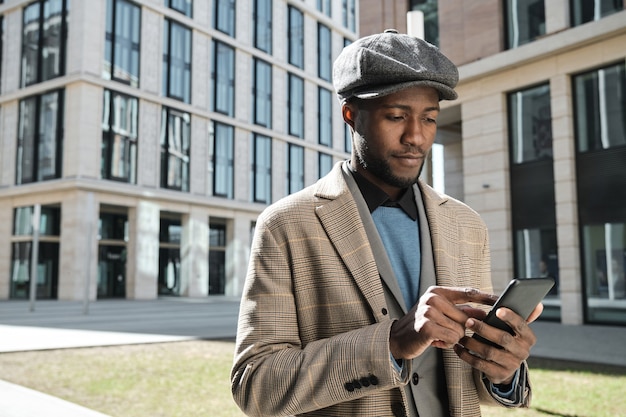 Afrikanischer junger Mann, der während seines Spaziergangs in der Stadt eine Nachricht auf seinem Handy eintippt