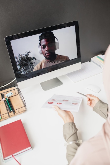 Afrikanischer Kerl auf dem Computerbildschirm, der den Lehrer ansieht, der Daten auf Papier erklärt