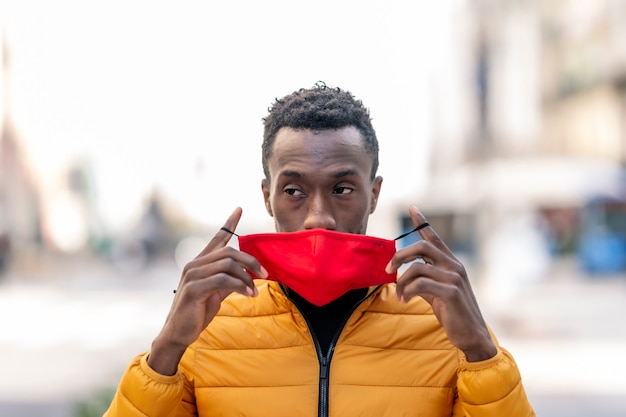 Afrikanischer Mann, der eine rote Gesichtsmaske mit nicht fokussiertem Stadthintergrund aufstellt