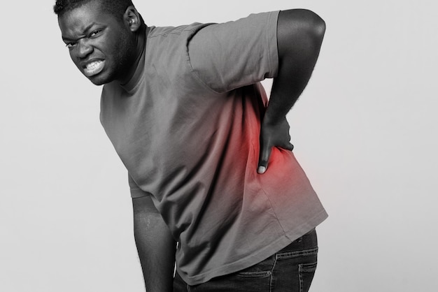 Afrikanischer Mann greift schmerzenden unteren Rücken mit rotem Fleck im Studio