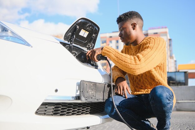 Afrikanischer Mann mit Ladekabel in der Nähe von Luxus-Elektroauto.