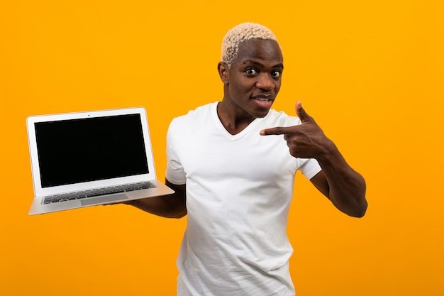 Afrikanischer Mann mit weißen Haaren lächelnd hält Laptop-Bildschirm vorwärts mit Layout, das auf Bildschirm auf gelb zeigt