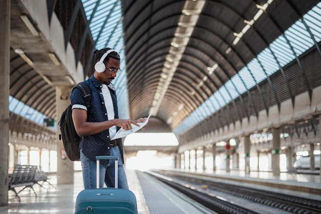 Afrikanischer Reisender, der eine Karte betrachtet, während er an einem Bahnhof wartet