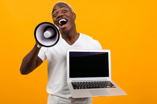 Afrikanischer schwarzer Mann mit weißen Haaren mit einem Megaphon und Laptop mit einem Modell auf einem gelben Studio