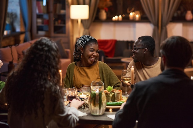 Afrikanisches junges Paar sitzt am Esstisch und lacht beim Treffen mit Freunden auf einer Dinnerparty