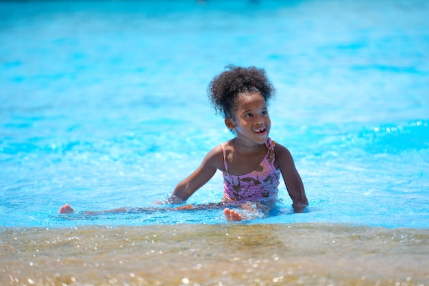 Afrikanisches Mädchen, das Wasser im Schwimmbad am Vergnügungspark sitzt und spielt.