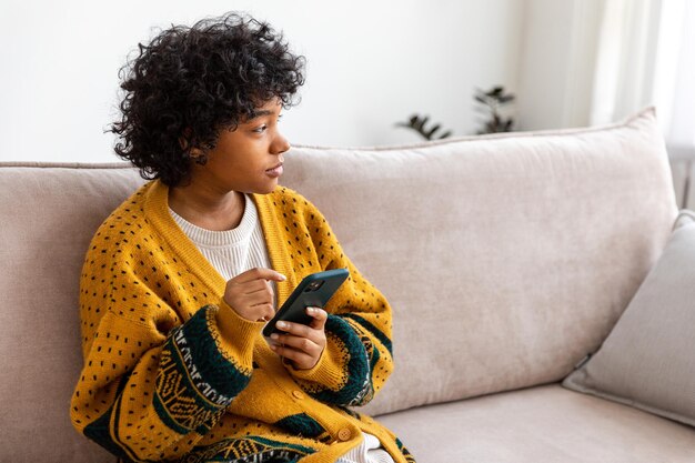 Afrikanisches Mädchen mit Smartphone-Touchscreen-Eingabe-Scroll-Seite zu Hause Frau mit Handy surfin