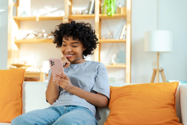 Afrikanisches Mädchen mit Smartphone-Touchscreen-Eingabe-Scroll-Seite zu Hause Frau mit Handy surfin