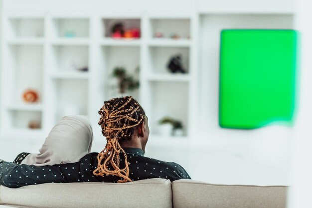 Afrikanisches Paar, das auf dem Sofa sitzt und gemeinsam fernsieht, Chroma-Green-Screen-Frau mit islamischem Hijab