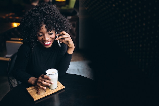 Afro americana mulher com telefone e café no café