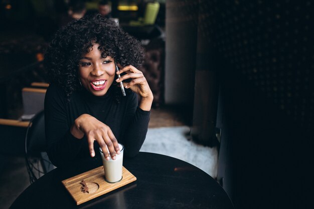 Afro americana mulher com telefone e café no café