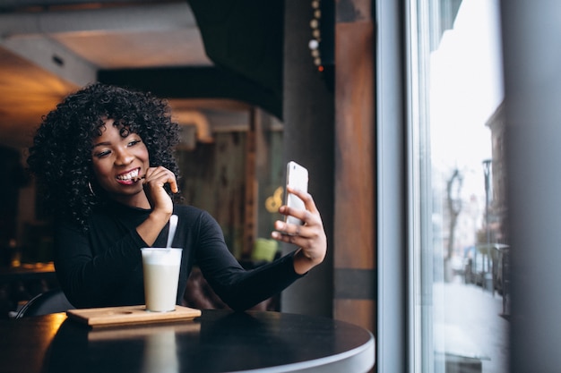 Afro americana mulher fazendo selfie e tomando café no café