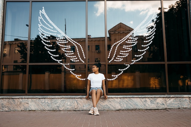 Foto afro americana mulher sentada na vitrine de vidro com asas de anjo