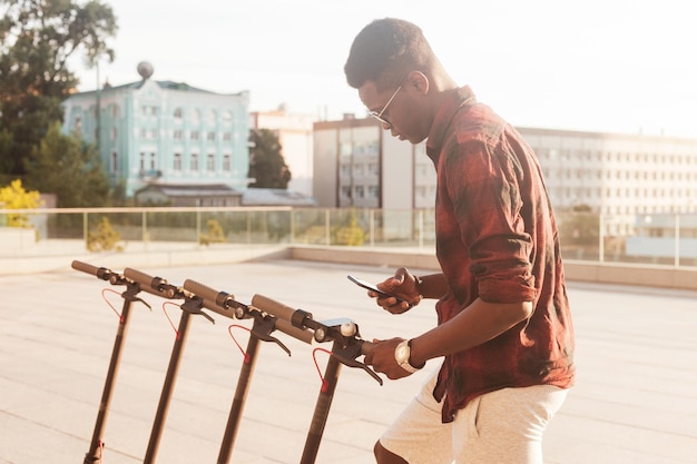 Afro-americano alugando uma scooter elétrica na rua um estudante verifica o transporte ecológico