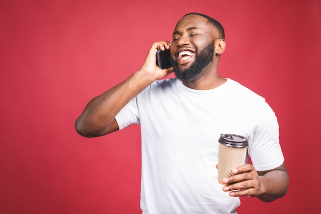 Afro-americano bonito com telefone móvel e tirar a xícara de café. Isolado sobre o fundo vermelho.