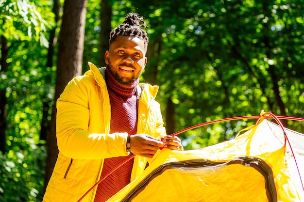 Afro-americano em jacker amarelo colocando uma barraca na floresta