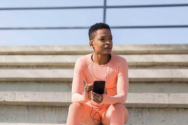 Afro-Amerikanerin müde nach dem Training, das Musik und Audio-Podcast hört, nach dem Joggen und Training im Stadion am Morgen