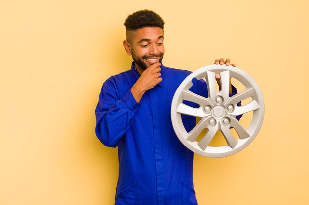 Afro-cooler Mann, der mit einem glücklichen, selbstbewussten Ausdruck lächelt, mit der Hand am Kinn, Fahrradmechaniker-Konzept