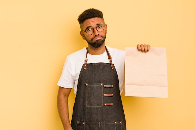 Afro-cooler Mann, der sich traurig und weinerlich fühlt, mit einem unglücklichen Blick und einem weinenden Lieferboten und einem Fast-Food-Konzept