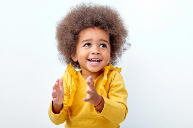 Afro flauschiges Kindermädchen klatscht und applaudiert glücklich und freudig lächelnd entzückendes charmantes Kind in Gelb ...
