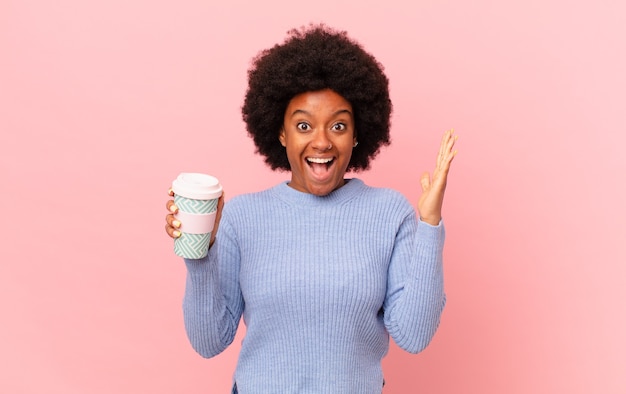 Afro-Frau, die sich glücklich, aufgeregt, überrascht oder schockiert fühlt, lächelt und über etwas Unglaubliches erstaunt ist. Kaffeekonzept