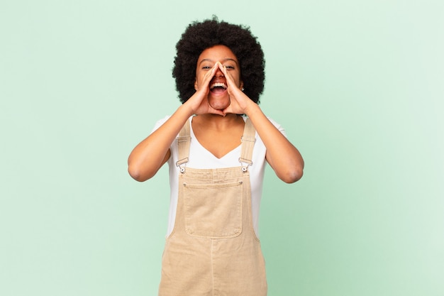 Afro-Frau, die sich glücklich, aufgeregt und positiv fühlt, mit den Händen neben dem Mund einen großen Schrei ausspricht und das Kochkonzept ausruft