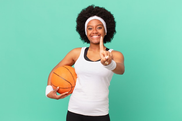 Afro-Frau, die stolz und selbstbewusst lächelt und die Nummer eins triumphierend posiert und sich wie ein Anführer fühlt. Basketball-Konzept