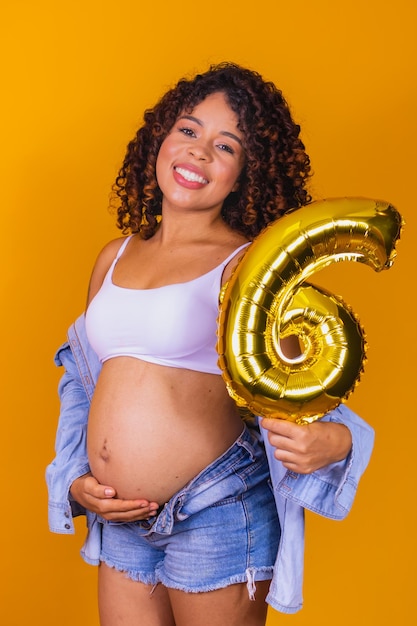 Afro-Frau im sechsten Monat schwanger mit einem Ballon mit der Nummer sechs