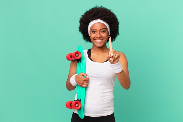 Afro-Frau lächelt und sieht freundlich aus, zeigt Nummer eins oder zuerst mit der Hand nach vorne und zählt herunter. Skateboard-Konzept