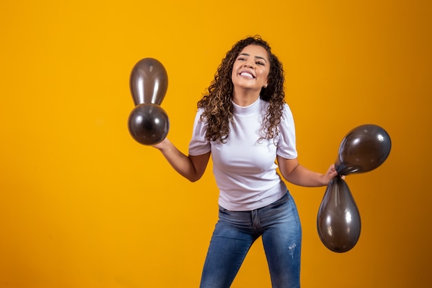 Afro-Frau mit schwarzen Ballons, die Geburtstagsangebote feiert. Black Friday-Verkauf