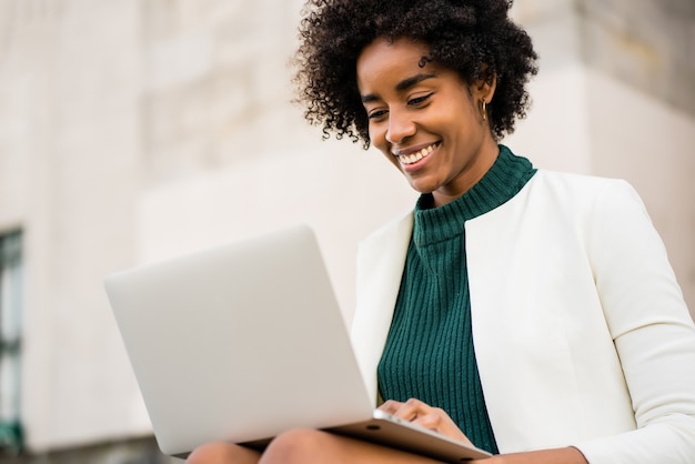 Afro-Geschäftsfrau, die ihren Laptop beim Sitzen auf Treppen im Freien verwendet.