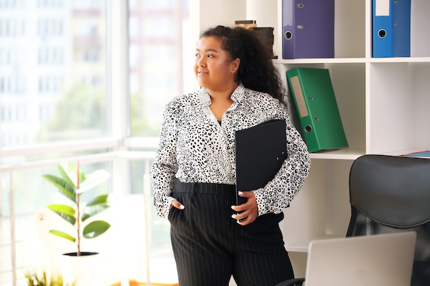 Afro-Geschäftsfrau im Hemd, das am Tisch am Fenster sitzt und Laptop im Büro benutzt.